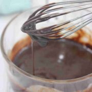 Dairy-free chocolate ganache dripping off a whisk over a glass bowl with more ganache in it.