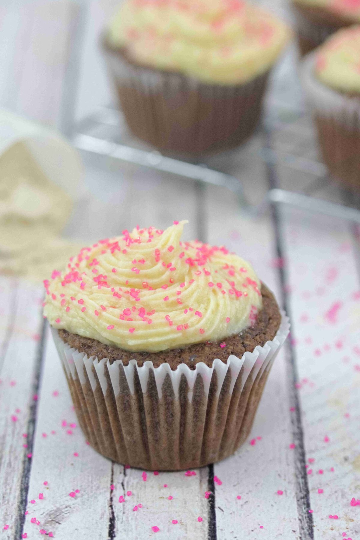 Chocolate protein cupcakes topped with vanilla buttercream frosting with pink sprinkles.