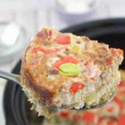 Close up of a slice of egg casserole being held over a black slow cooker of breakfast casserole.