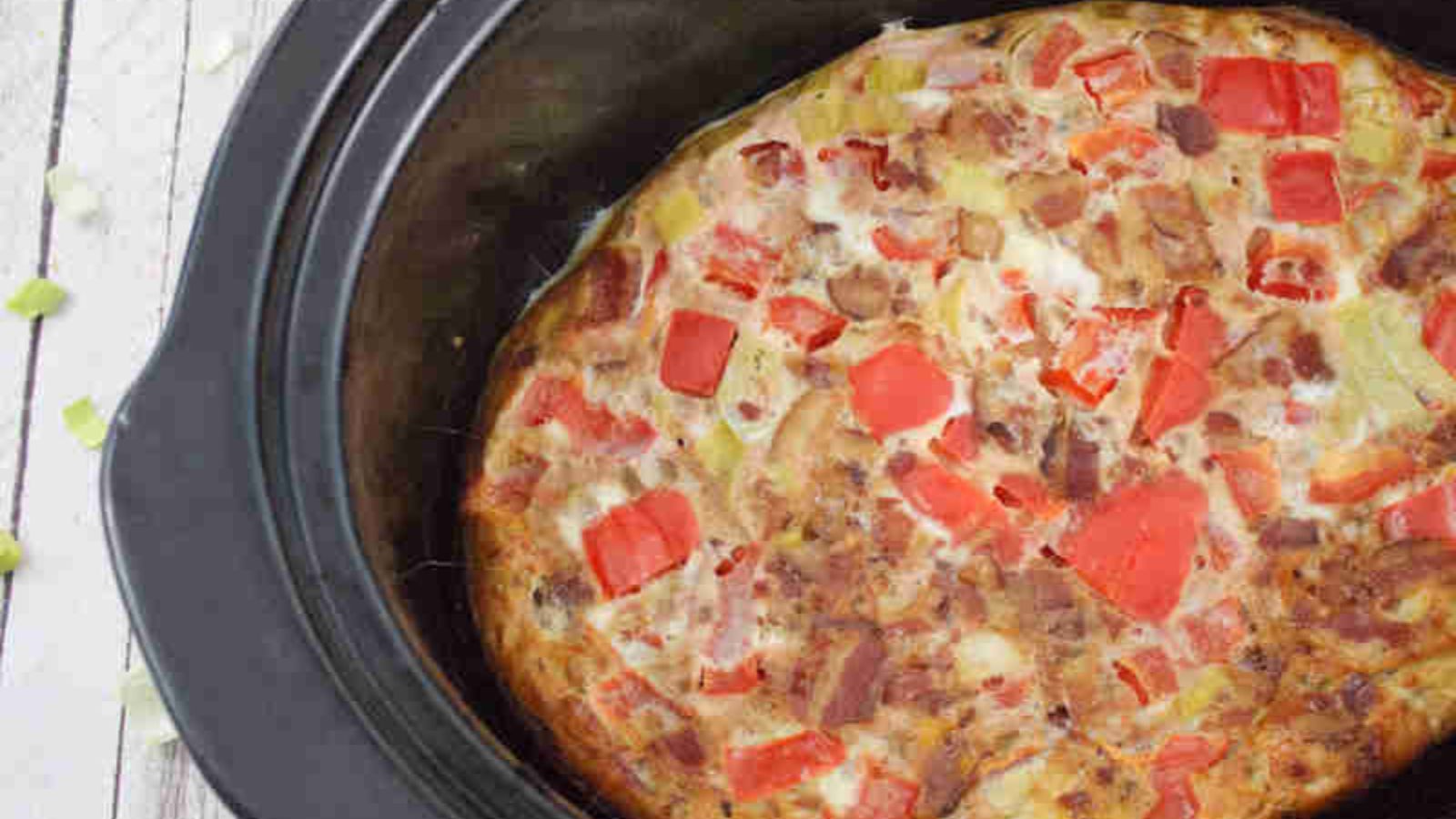 Black slow cooker with an egg casserole in it with red bell peppers.