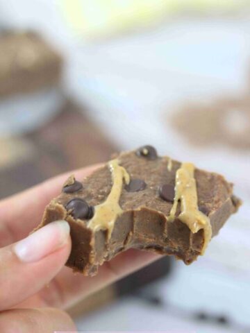 Close up image of fingers holding a piece of chocolate protein fudge with a bite taken out.