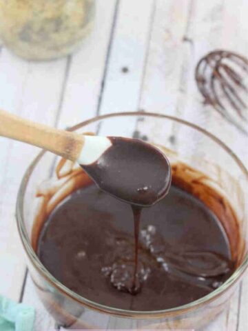 Dairy-free chocolate ganache dripping off a white spoon over a glass bowl.