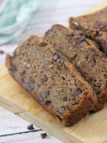 Chocolate protein zucchini bread sliced on a cutting board with chocolate chips around it.