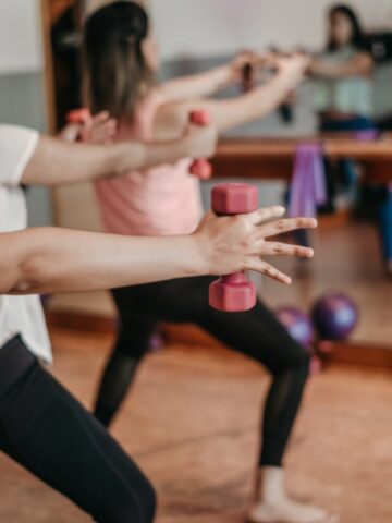 Close up of multiple arms in a fitness class holding small dumbbells.