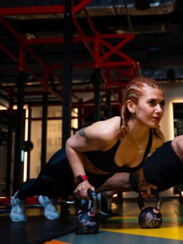 A man and a woman performing push ups on kettlebells.