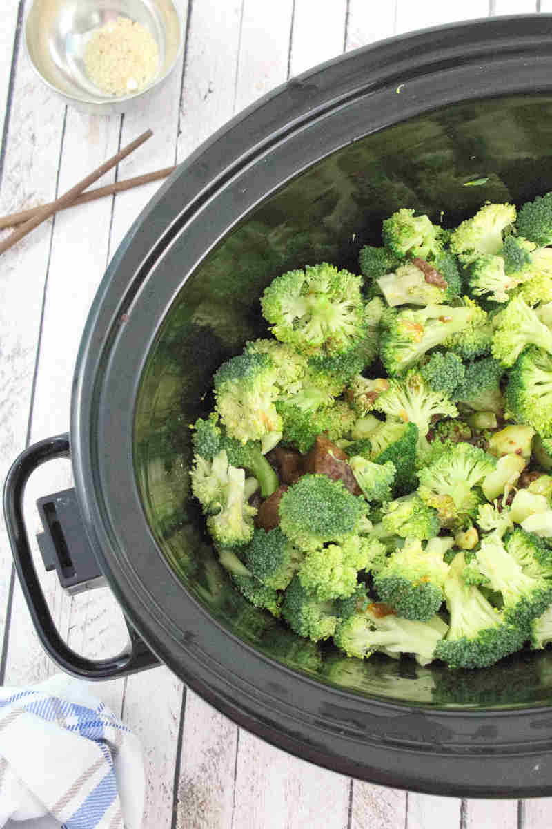 A black slow cooker with broccoli on top of beef.