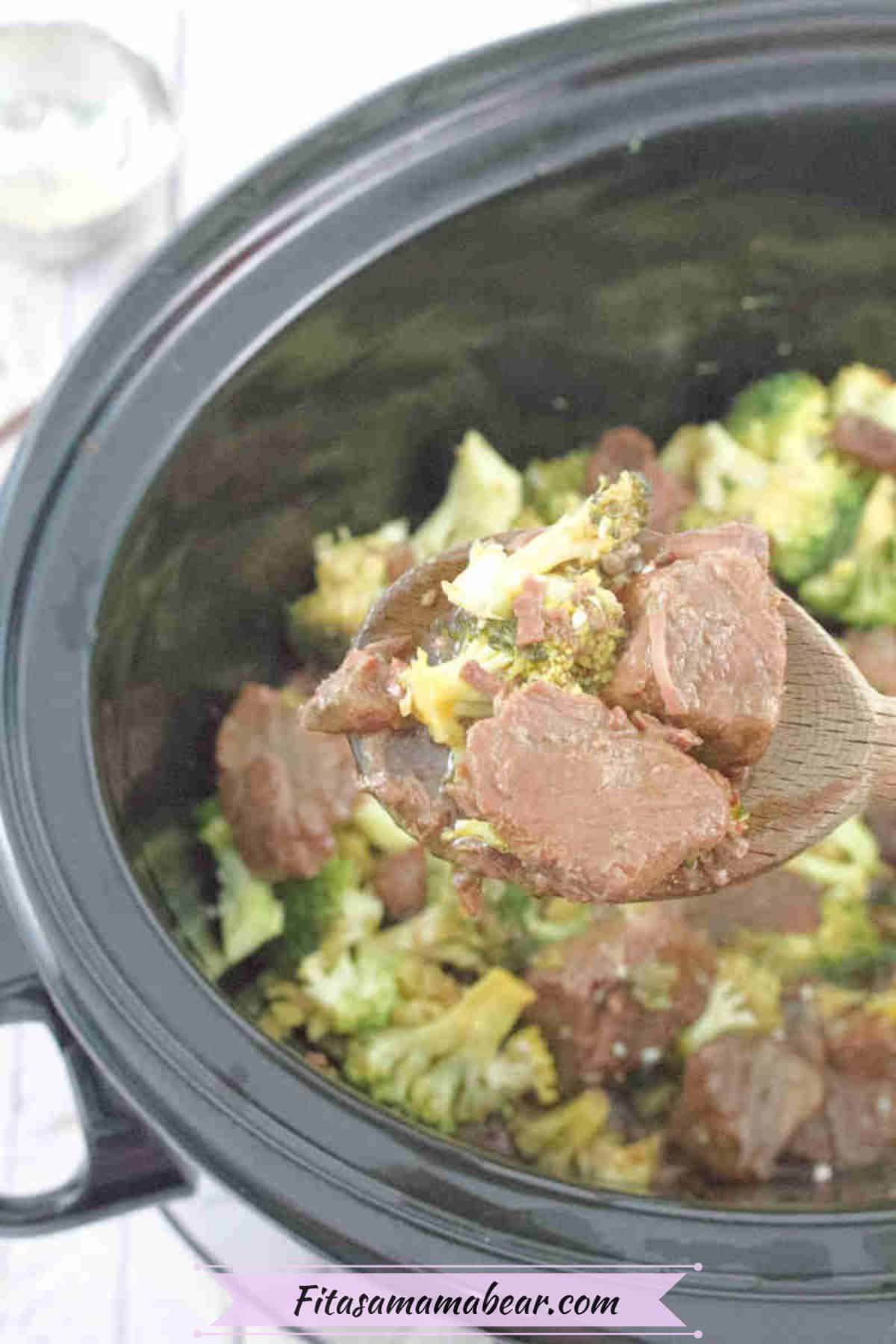 Black slow cooker with beef and broccoli in it and a wooden spoon holding some of the gluten-free beef and broccoli.