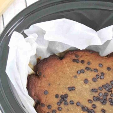 Black slow cooker lined with parchment paper and high protein banana bread with chocolate chips in it.
