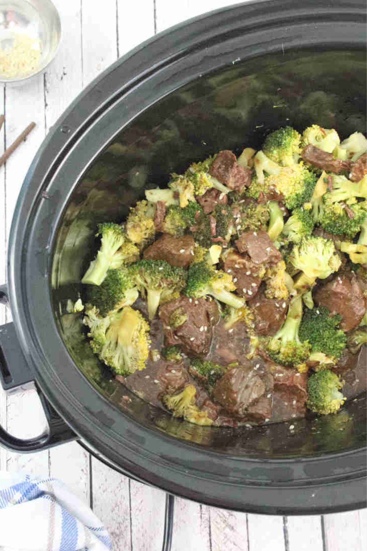 Black slow cooker with beef and broccoli in it.