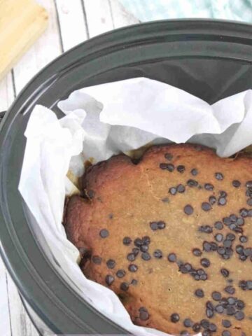 Black slow cooker lined with parchment paper and high protein banana bread with chocolate chips in it.
