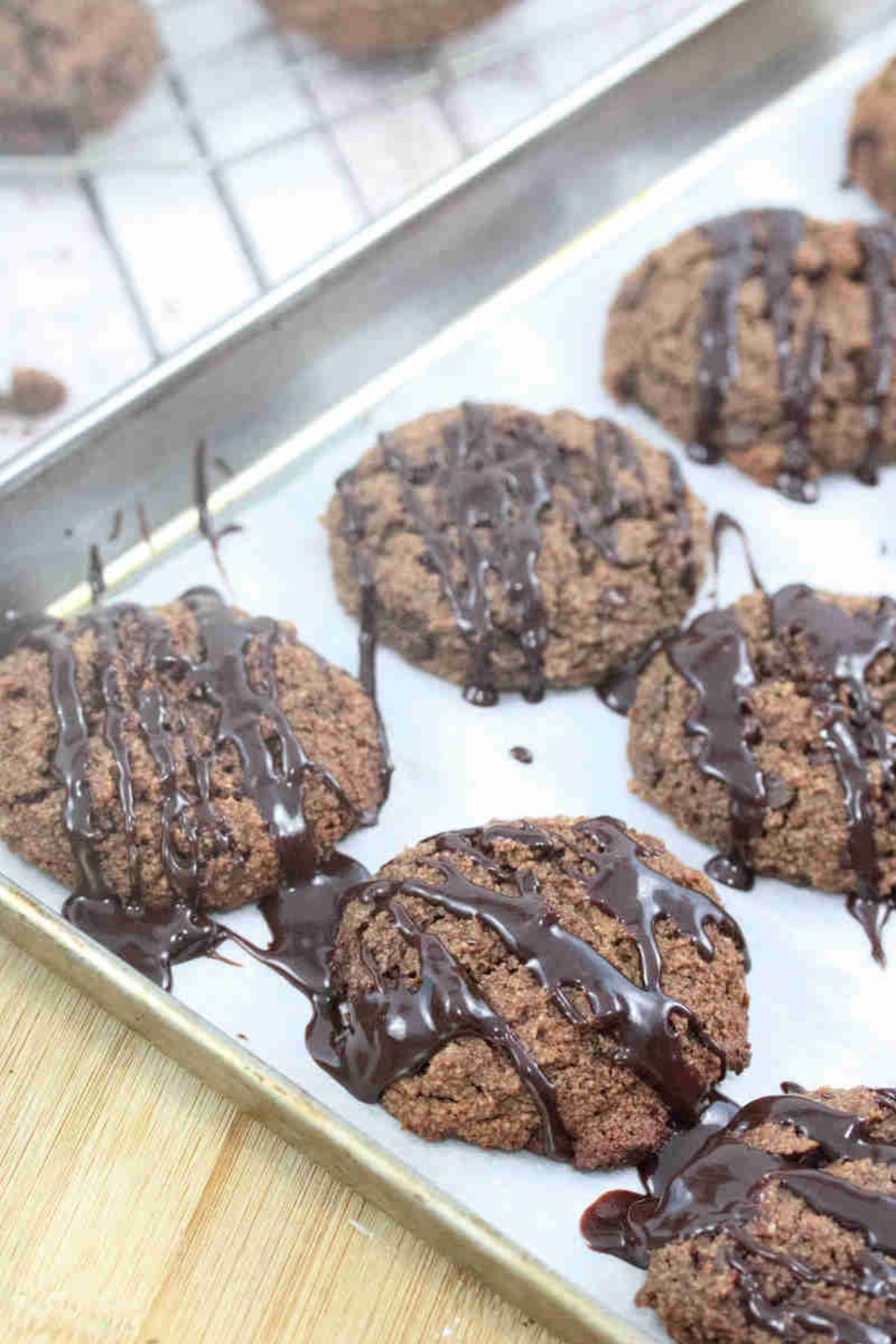 Chocolate almond flour cookies drizzled with chocolate on a piece of parchment paper on a baking sheet.