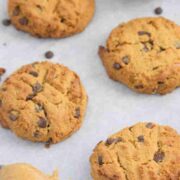 Peanut butter chocolate chip protein cookies on a parchment paper lined baking tray with a spoon of peanut butter on the tray too.