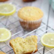 Lemon protein muffins on a cooling rack with lemons around them and one muffin broken in half.