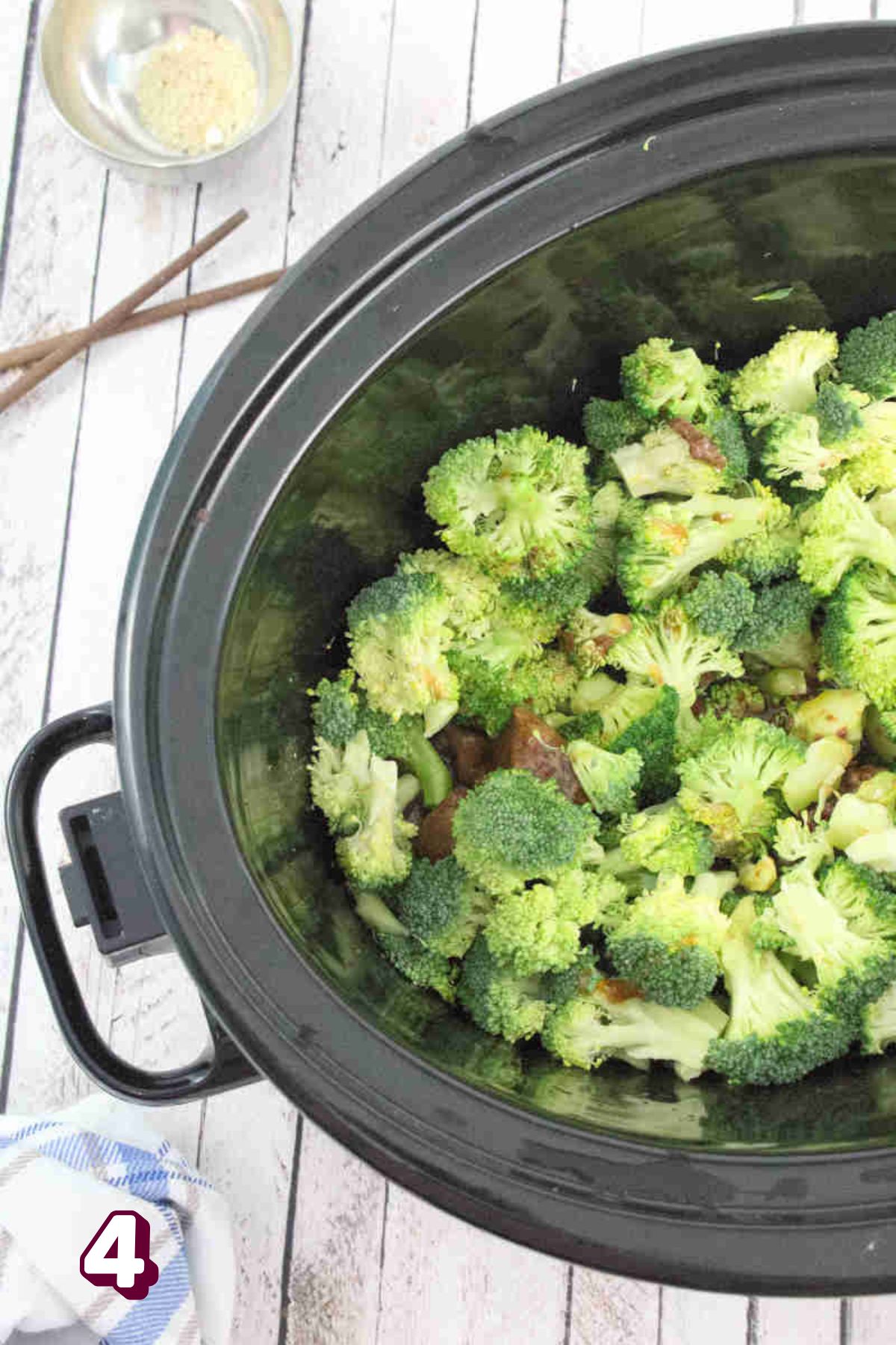 A black slow cooker with broccoli on top of beef.