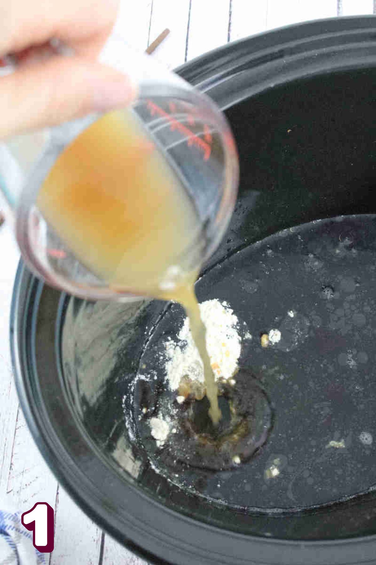 Chicken broth being poured into a black slow cooker.
