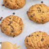 Peanut butter chocolate chip protein cookies on a parchment paper lined baking tray with a spoon of peanut butter on the tray too