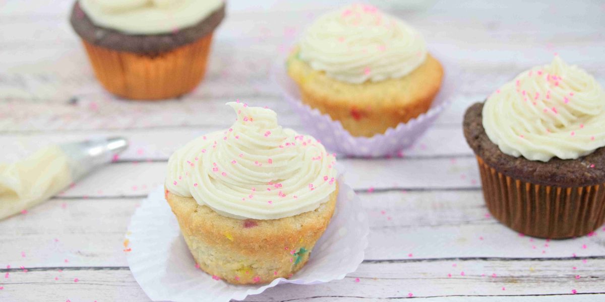 Four cupcakes lined up topped with protein frosting and a piping bag beside them.