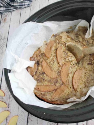 Black slow cooker lined with parchment paper and protein oatmeal inside of it with a wooden spoon.