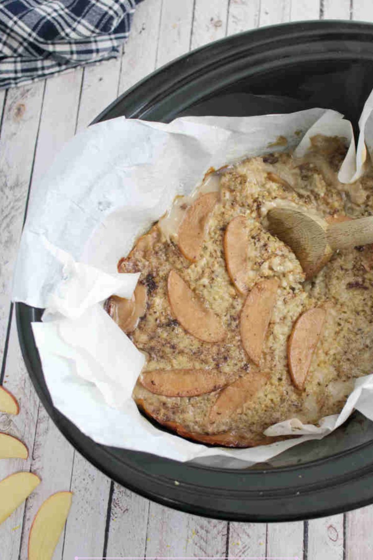 Black slow cooker lined with parchment paper and protein oatmeal inside of it with a wooden spoon.