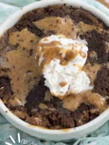 Chocolate protein pwoder mug cake topped with peanut butter and coconut whippe cream in a white mug on a blue linen.