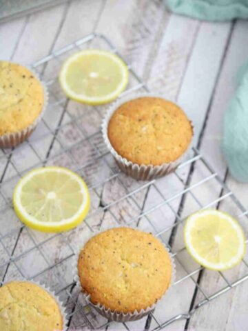 Lemon protein muffins on a cooling rack with lemons around them.