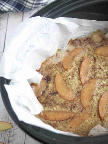 Black slow cooker lined with parchment paper and protein oatmeal inside of it with a wooden spoon.