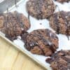 Chocolate almond flour cookies drizzled with chocolate on a piece of parchment paper on a baking sheet.
