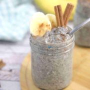 Banana chia pudding in a mason jar with a spoon in it and sliced bananas, and cinnamon on top and the jar on a wooden board.