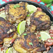 Gluten-free jerk chicken and rice in a cast iron skillet with limes on it.
