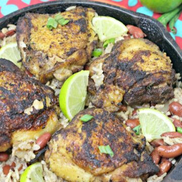 Gluten-free jerk chicken and rice in a cast iron skillet with limes on it.