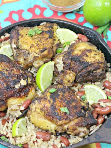 Gluten-free jerk chicken and rice in a cast iron skillet with limes on it.