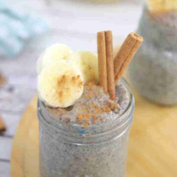 Banana chia pudding in a mason jar with a spoon in it and sliced bananas, and cinnamon on top and the jar on a wooden board.