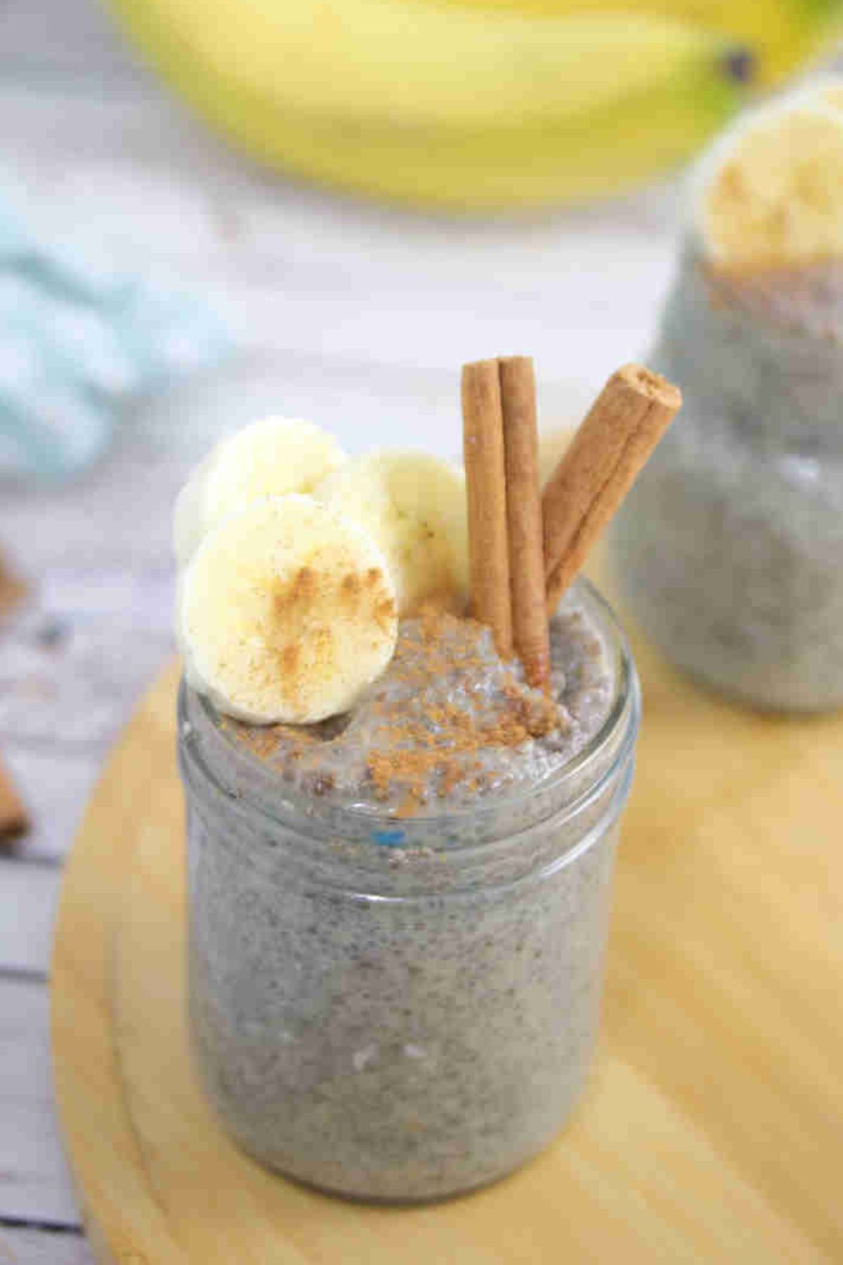 Banana chia pudding in a mason jar with a spoon in it and sliced bananas, and cinnamon on top and the jar on a wooden board.