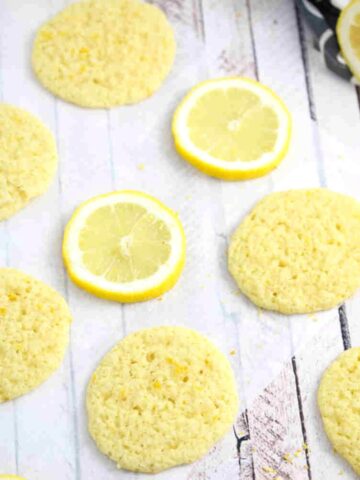 Thin dairy and gluten-free lemon cookies on parchment paper with lemons around them.