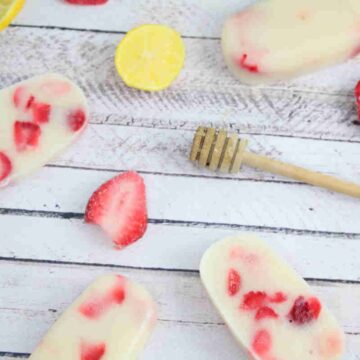 Strawberry yogurt protein popsicles laying flat with strawberries, a honey stick, and lemons around them.