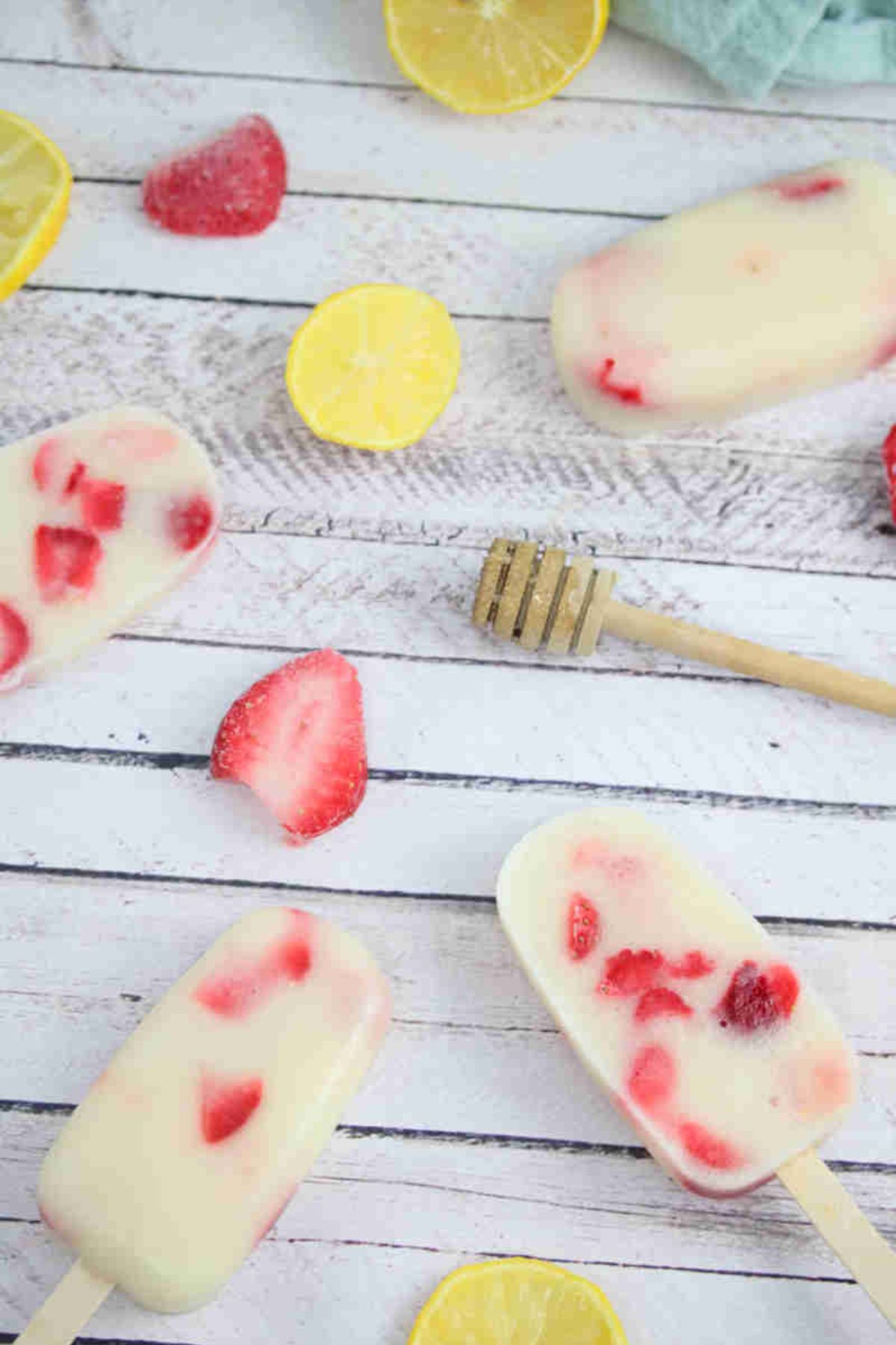 Strawberry yogurt protein popsicles laying flat with strawberries, a honey stick, and lemons around them.