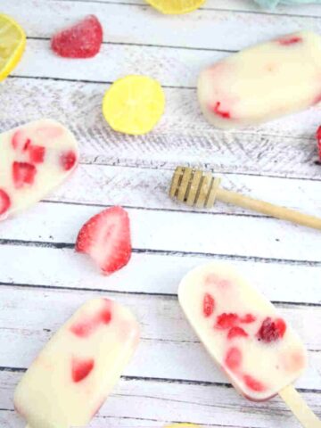 Strawberry yogurt protein popsicles laying flat with strawberries, a honey stick, and lemons around them.