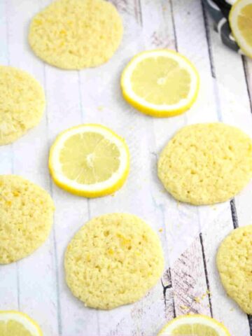Thin dairy and gluten-free lemon cookies on parchment paper with lemons around them.