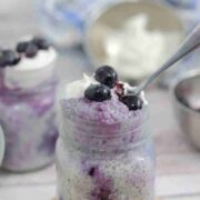 Blueberry chia pudding in a small mason jar on a cutting board with a spoon in the jar.