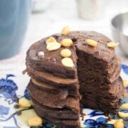 Blue and white plate with chocolate protein pancakes topped with peanuts with a coffee mug and silver bowl behind them.
