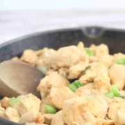 Spicy chicken bites in a cast iron skillet with green onions on top and a wooden spoon in the pan.