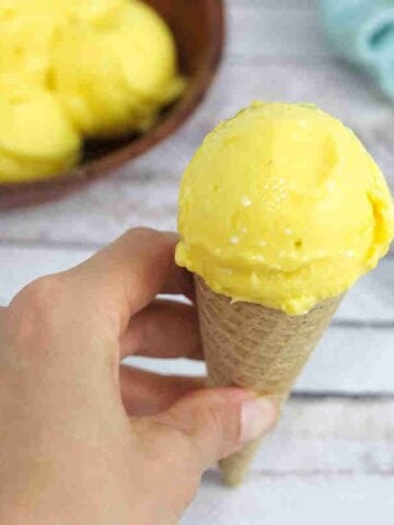 Close up of homemade mango ice cream in a gluten-free cone being held between fingers.