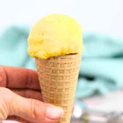 Close up of homemade mango ice cream in a gluten-free cone being held between fingers.