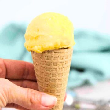 Close up of homemade mango ice cream in a gluten-free cone being held between fingers.