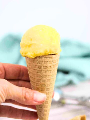 Close up of homemade mango ice cream in a gluten-free cone being held between fingers.