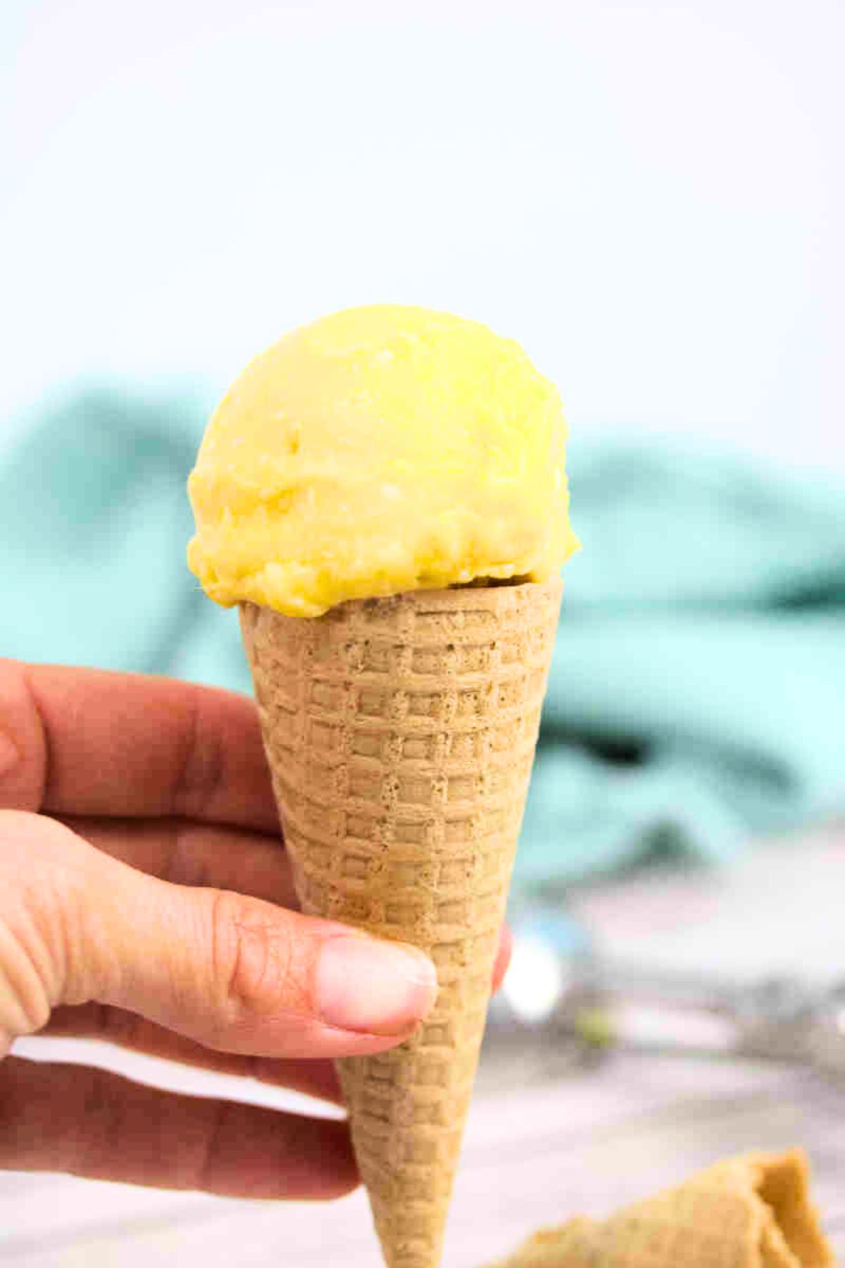 Close up of homemade mango ice cream in a gluten-free cone being held between fingers.