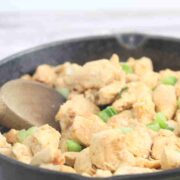 Spicy chicken bites in a cast iron skillet with green onions on top and a wooden spoon in the pan.