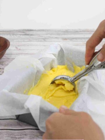 Homemade mango ice cream in a parchment paper lined pan with an ice cream scoop in it.
