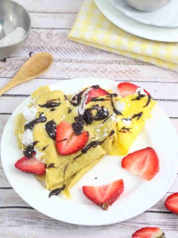 Protein crepes drizzled with chocolate on a white plate with strawberries on it.