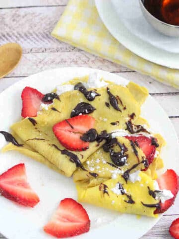 Protein crepes drizzled with chocolate on a white plate with strawberries on it
